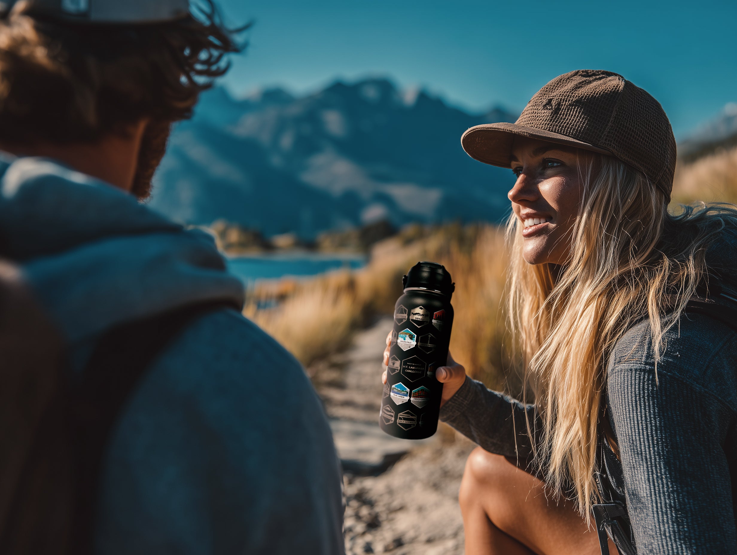 Two people sitting outdoors with mountains in the background, one holding a water bottle.